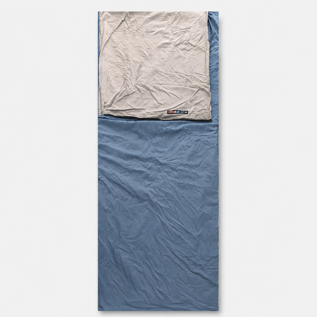 Ein hellblauer Schlafsack im ausgebreiteten Zustand mit grauem Kopfteil und eingenähtem Etikett.