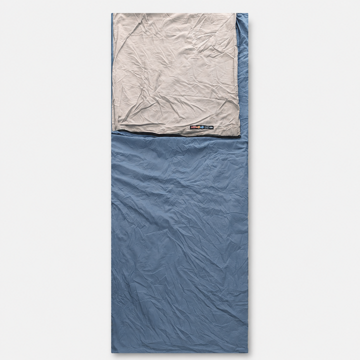 Ein hellblauer Schlafsack im ausgebreiteten Zustand mit grauem Kopfteil und eingenähtem Etikett.