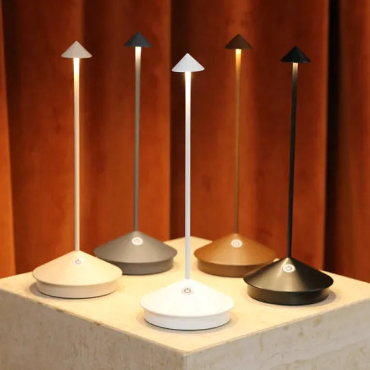 Moderne LED-Tischlampen in verschiedenen Farben auf einem Podest vor braunem Hintergrund.