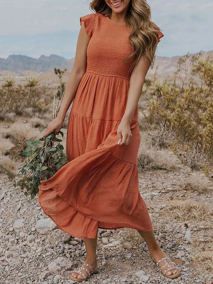 Frau in orangefarbenem Damenkleid mit Rüschenärmeln und Stufenrock, posiert in einer weiten Landschaft.