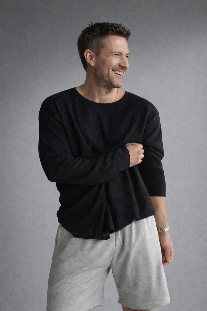 Mann präsentiert ein schwarzes Herren Strick-Oberteil kombiniert mit grauen Shorts