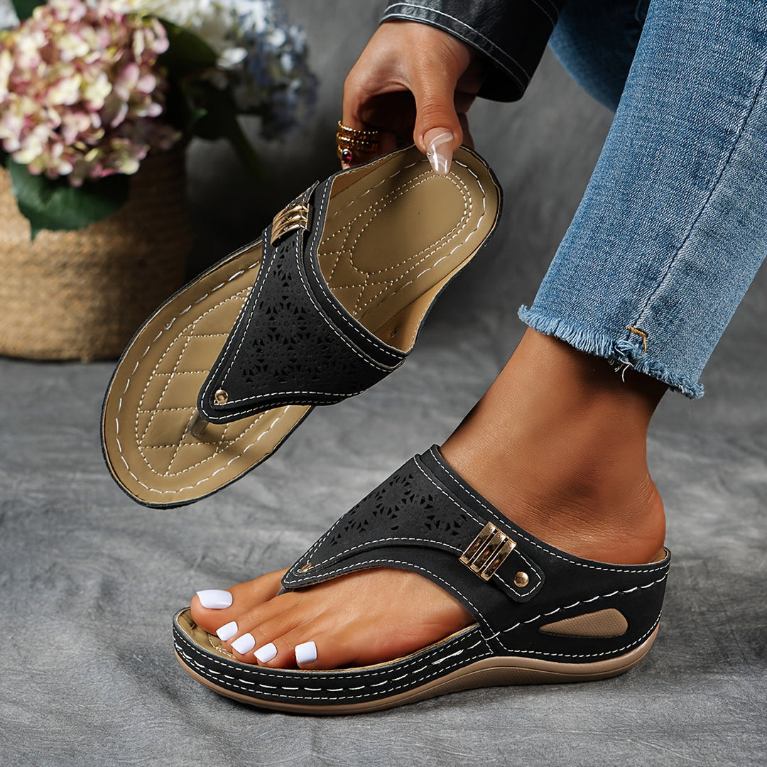 Dame trägt schwarze orthopädische Sandale mit goldenem Detail, hält die zweite Sandale.