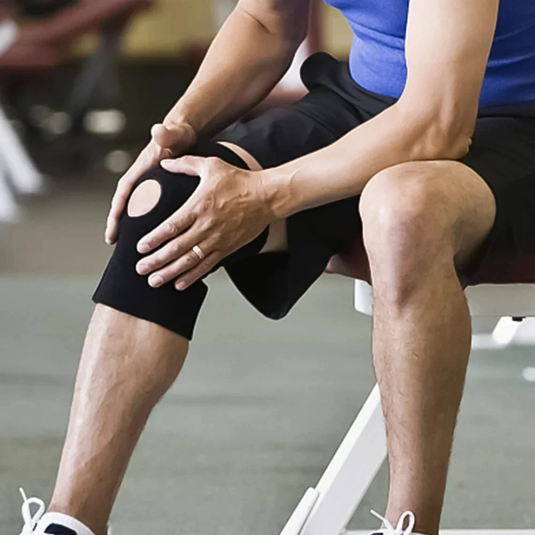 Mann sitzt auf einer Trainingsbank und trägt eine schwarze Knie-Stützbandage.