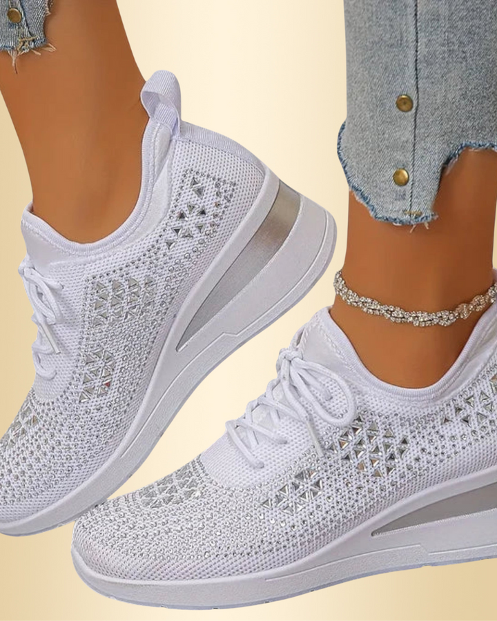Nahaufnahme von weißen Damen Glitzer-Sneakern mit Schnürung, getragen zu Jeans und Fußkettchen.