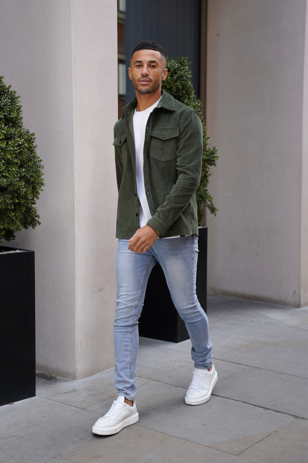 Ganzkörperansicht des Models in grünem Cordhemd und heller Jeans
