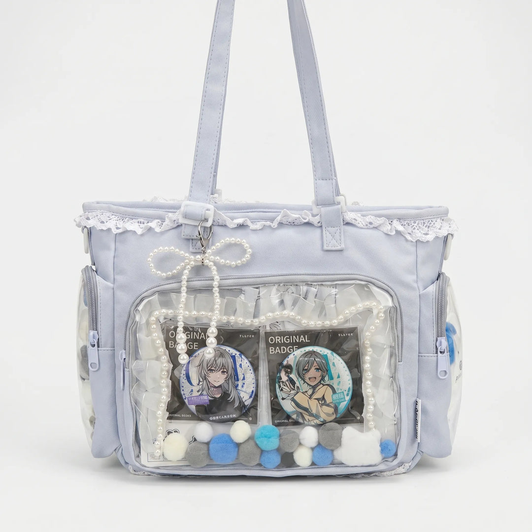 Graue Itabag Umhängetasche mit durchsichtigem Frontfenster und blauen Deko-Elementen vor weißem Hintergrund