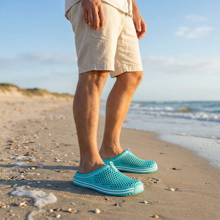 Person am Strand trägt türkise Badesandalen mit perforiertem Obermaterial