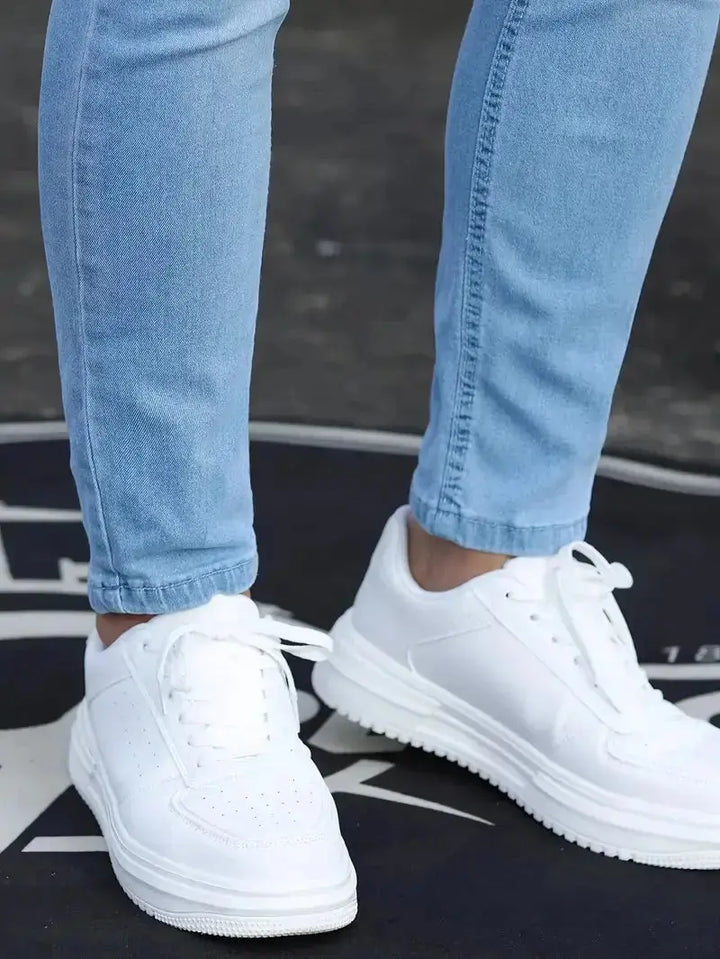 Nahaufnahme der hellblauen Herrenjeans am Bein mit weissen Schuhen