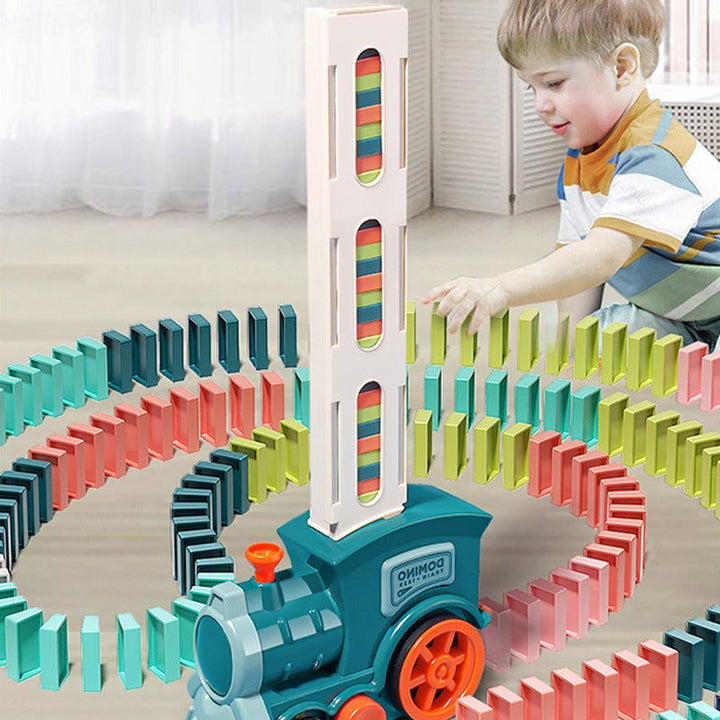 Junge spielt mit buntem Domino-Zugspielzeug, das Dominosteine aufstellt.