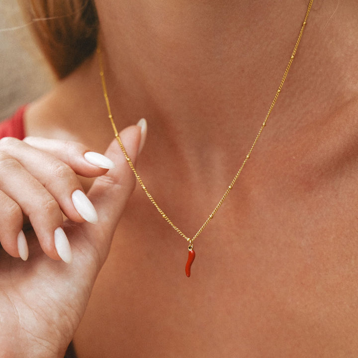 Frauenhand hält die goldene Halskette mit rotem Chili-Anhänger, Detail des Charms.