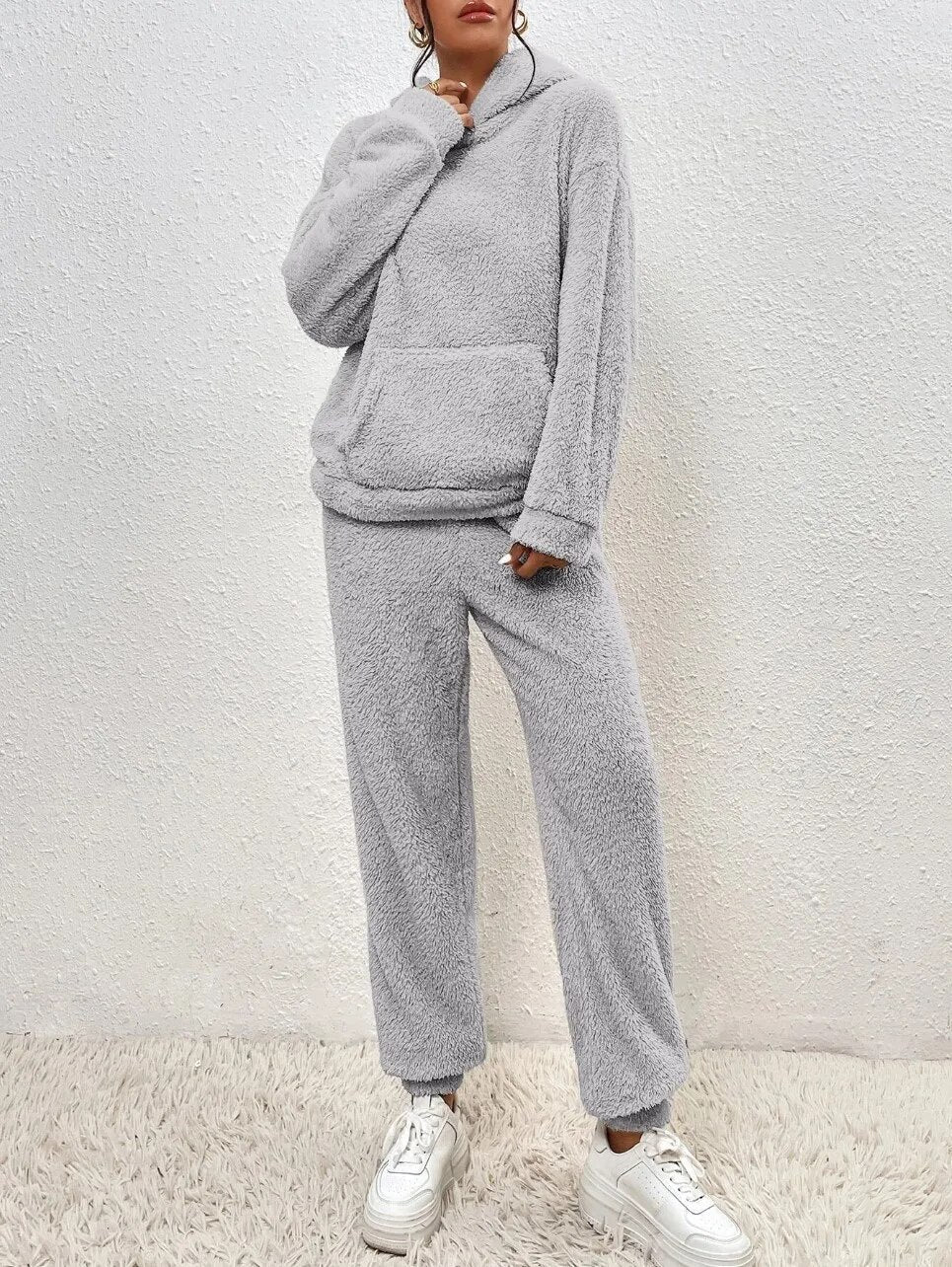 Frau trägt gemütlichen Damen Teddy-Hausanzug mit Kapuze beim Entspannen. Bequeme Freizeitkleidung und Homewear.