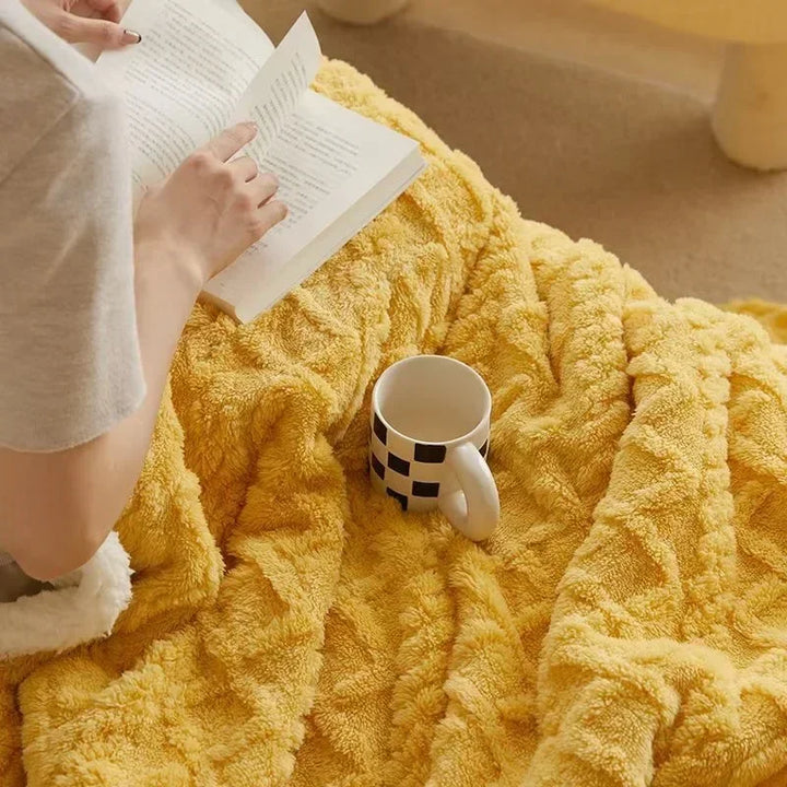 Person liest Buch unter gelber Kuscheldecke mit Tasse, gemütliche Leseecke, Entspannung.