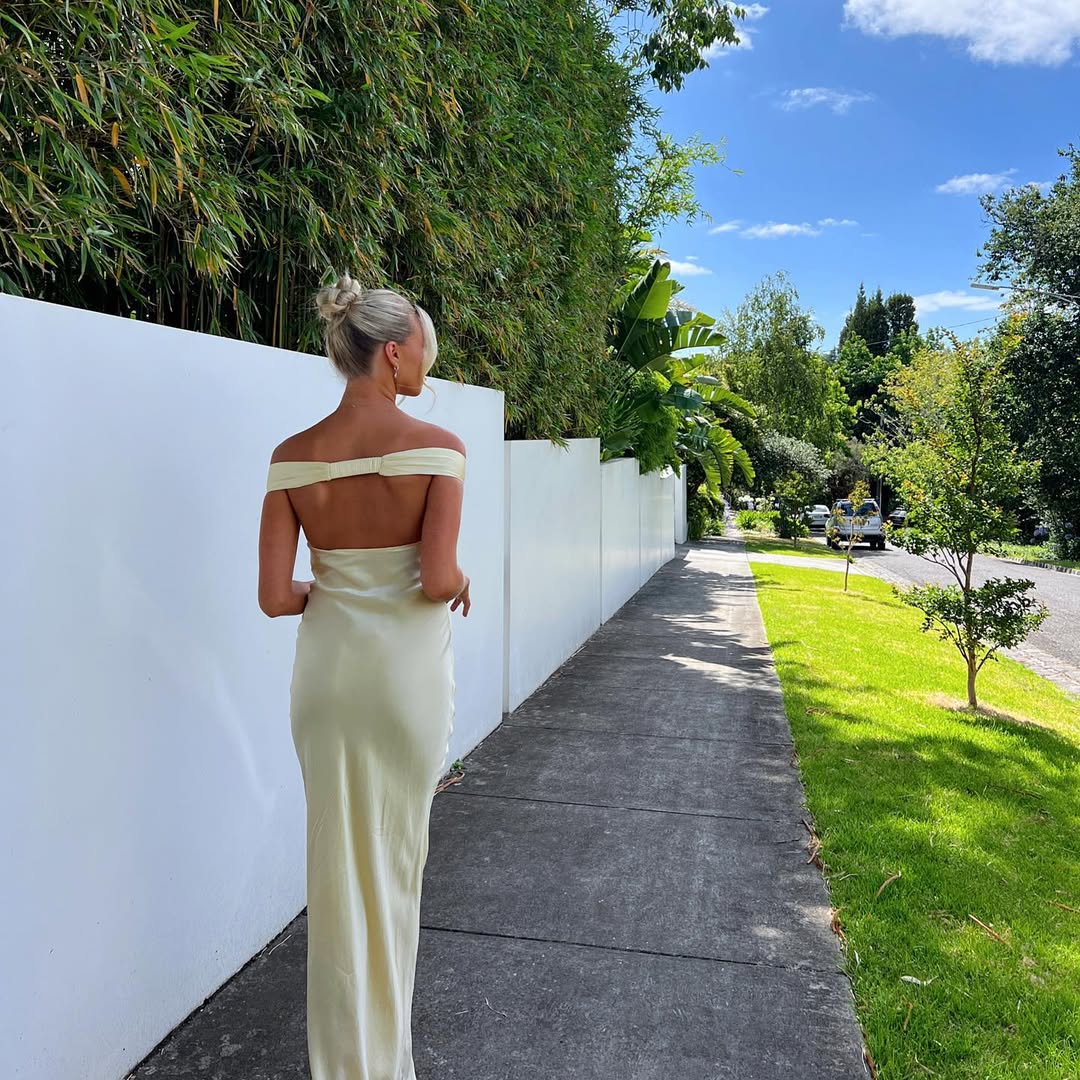 Frau trägt gelbes, figurbetontes Maxikleid mit offenem Rücken, elegant für Hochzeitsgäste oder Party.