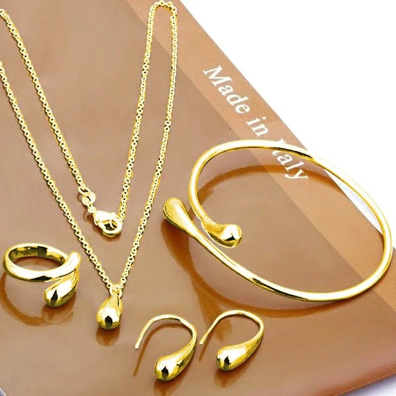 Goldene Schmuckset: Halskette, Armband, Ohrringe, Ringe auf braunem Hintergrund, Made in Italy.