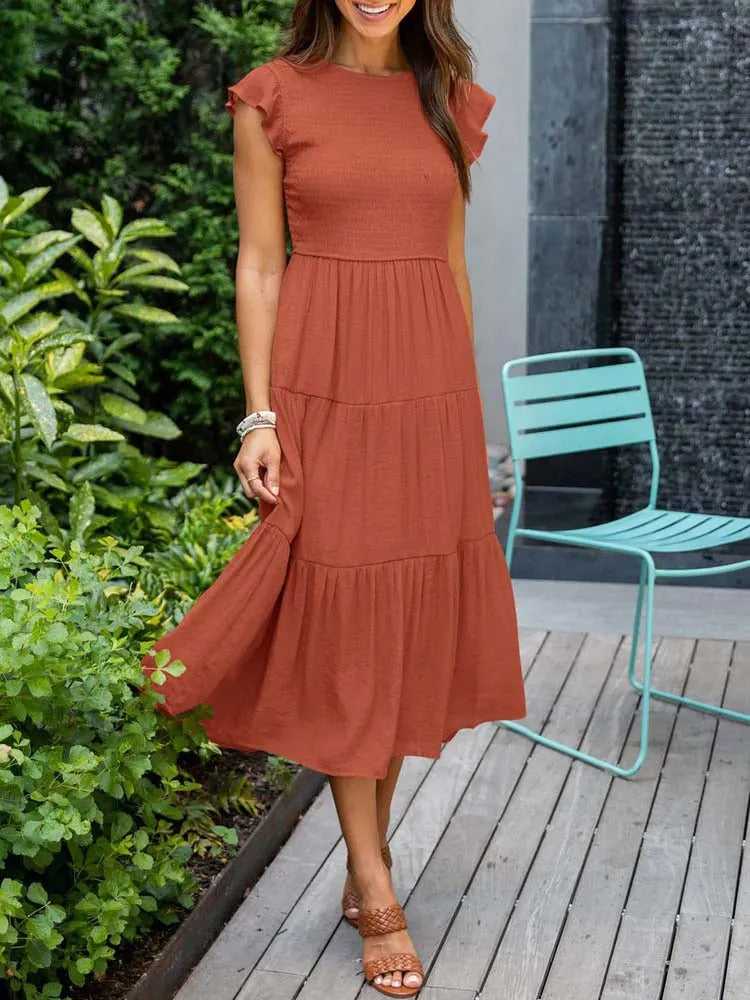 Elegantes orangefarbenes Sommerkleid an einer Frau, die auf einer modernen Holzterrasse im Garten steht.