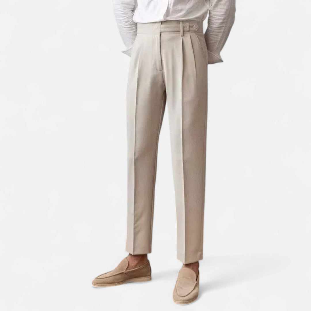 Nahaufnahme der Beine eines Mannes in beiger Chino Hose mit Bundfalten, Loafern und umgeschlagenen Ärmeln.