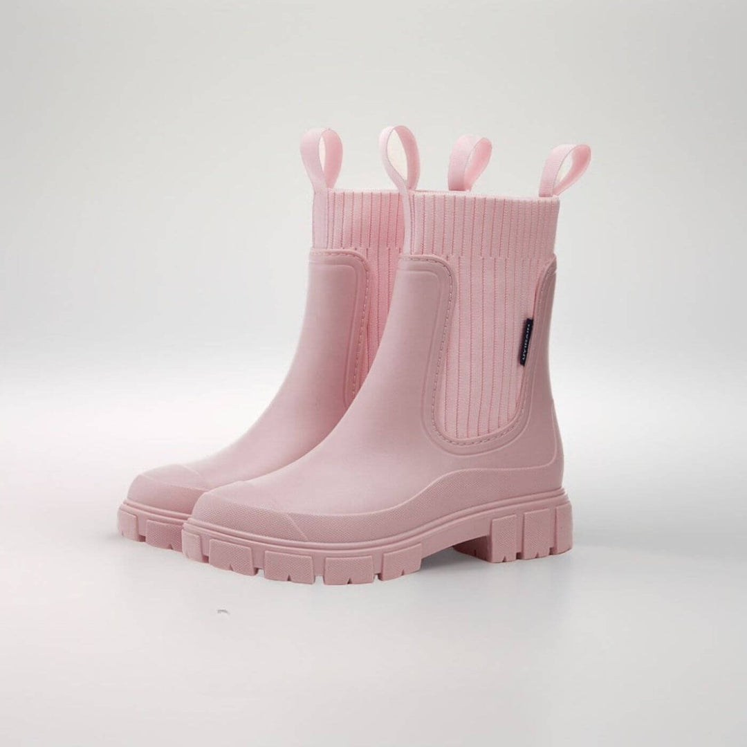 Frau trägt stylische, knöchelhohe Damen-Regenstiefel bei Regenwetter auf der Straße.