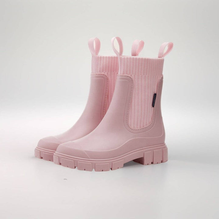 Frau trägt stylische, knöchelhohe Damen-Regenstiefel bei Regenwetter auf der Straße.