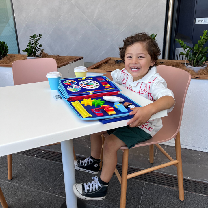 Kleinkind spielt mit farbenfrohem Montessori Beschäftigungsbrett, lernt spielerisch & fördert die Geschicklichkeit.