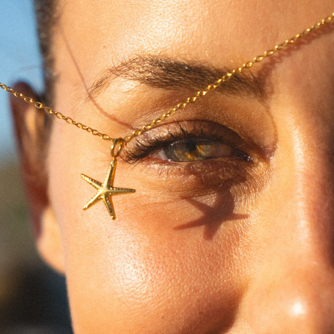 Nahaufnahme einer goldenen Seestern-Halskette nahe dem Gesicht