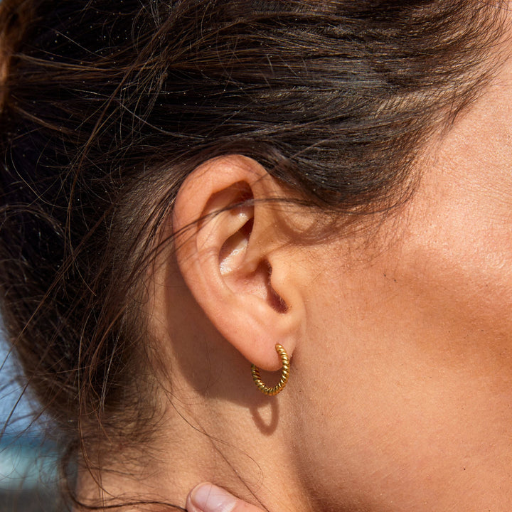 Damen Ohrläppchen mit kleinen gedrehten goldenen Creolen im Sonnenlicht